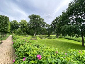 A garden with a paved walkway, variously sized trees, and flowering shrubs. - Holiday Home in Gravdal (Grasten)
