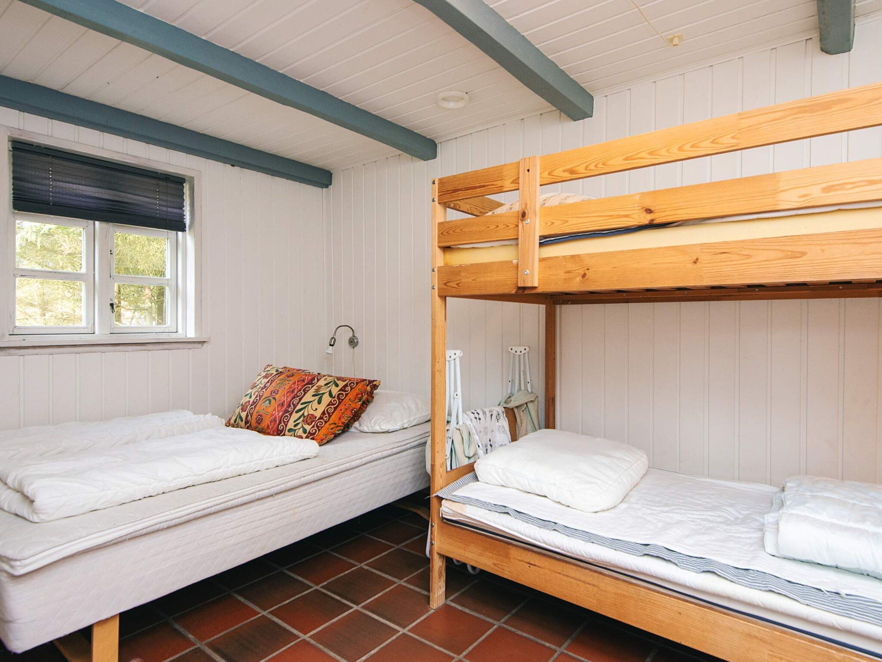 Ett rum med två våningssängar, ett fönster med persienner, en vit vägg och ett klinkergolv.