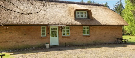 A single-story brick building with a thatched roof, a white door, and two windows with green frames.