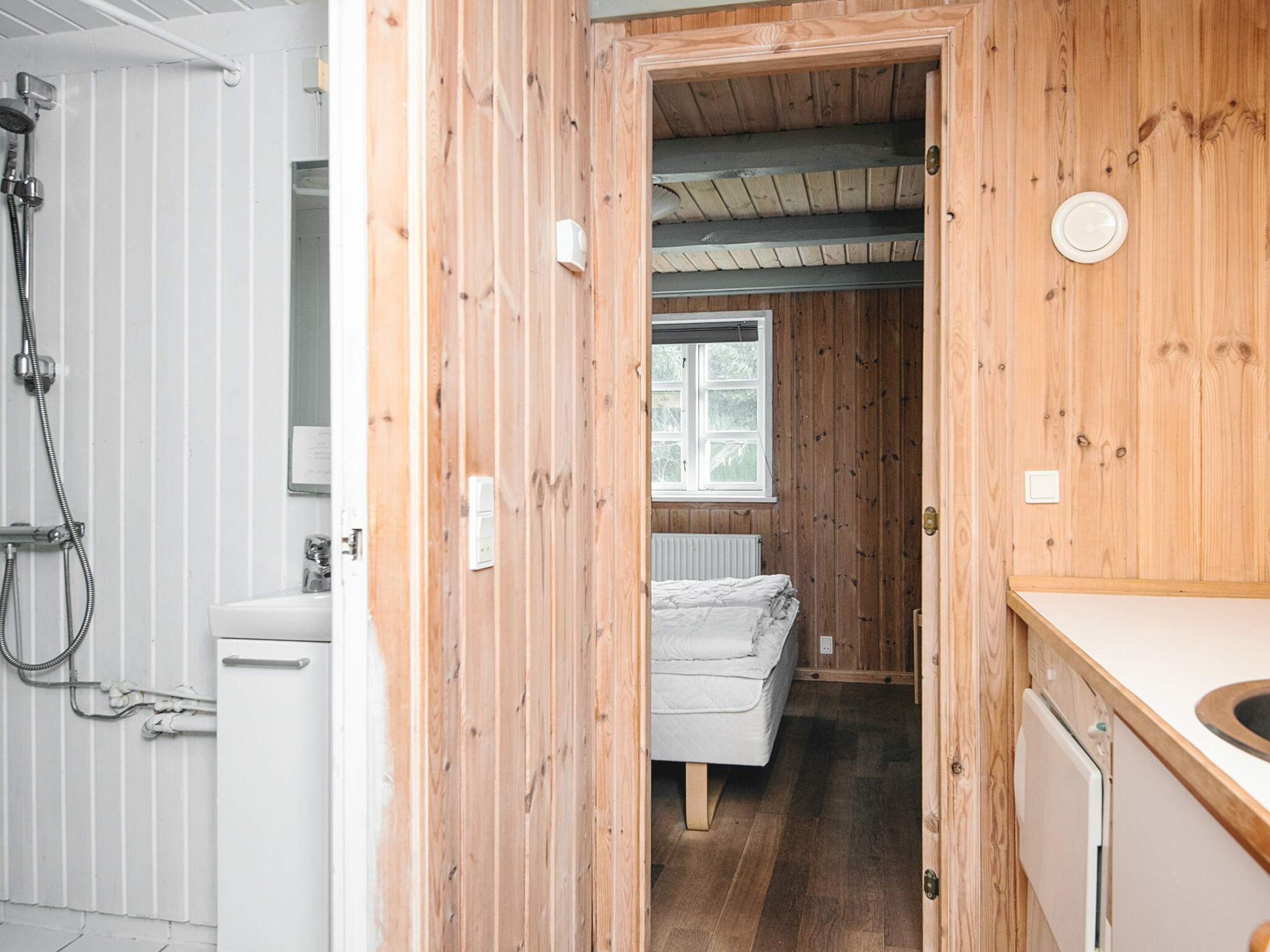A wooden interior with a shower, a bed, and a window.