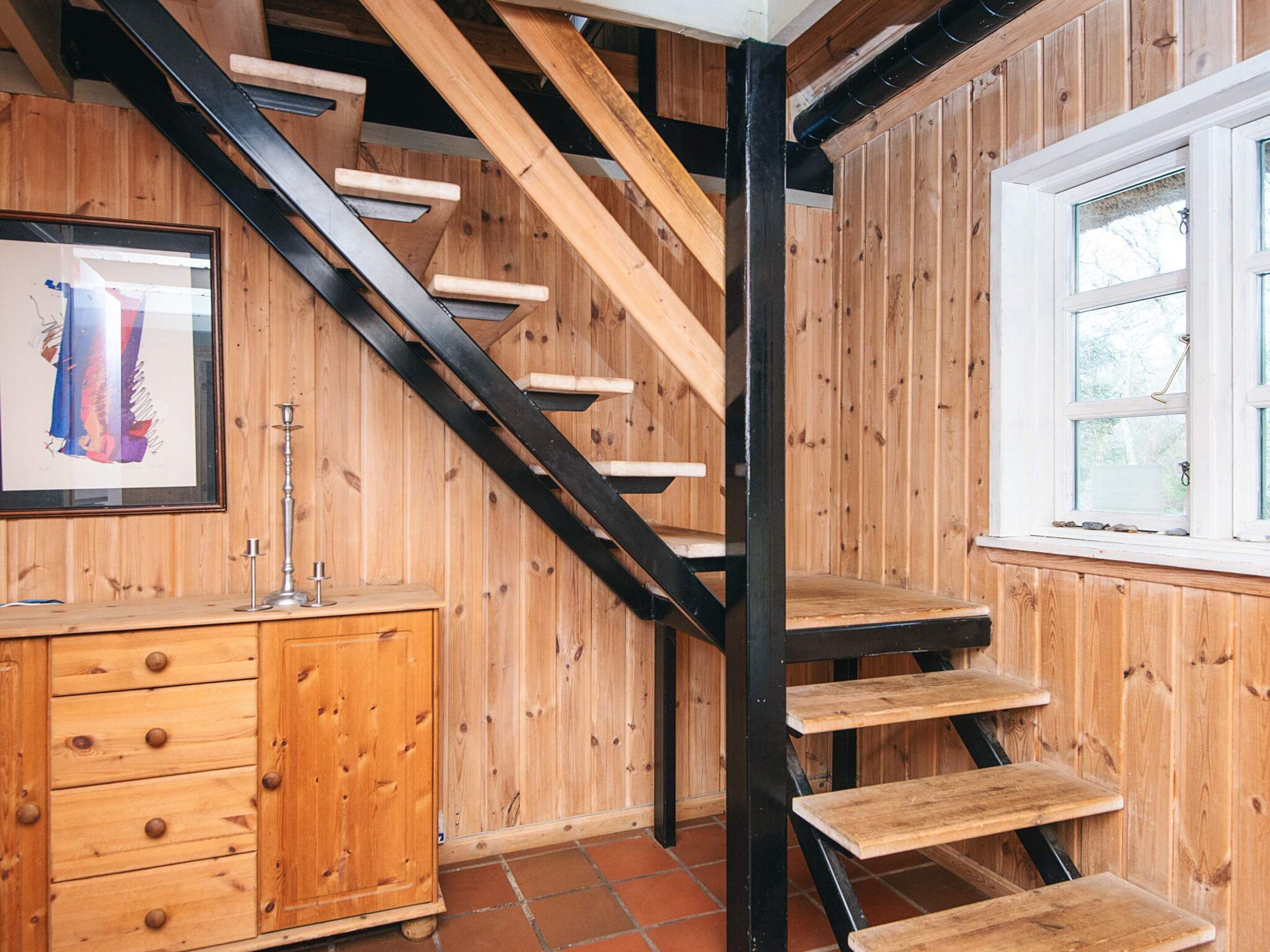 A wooden staircase with black metal railings, a wooden cabinet with drawers, and a window with a view of trees.