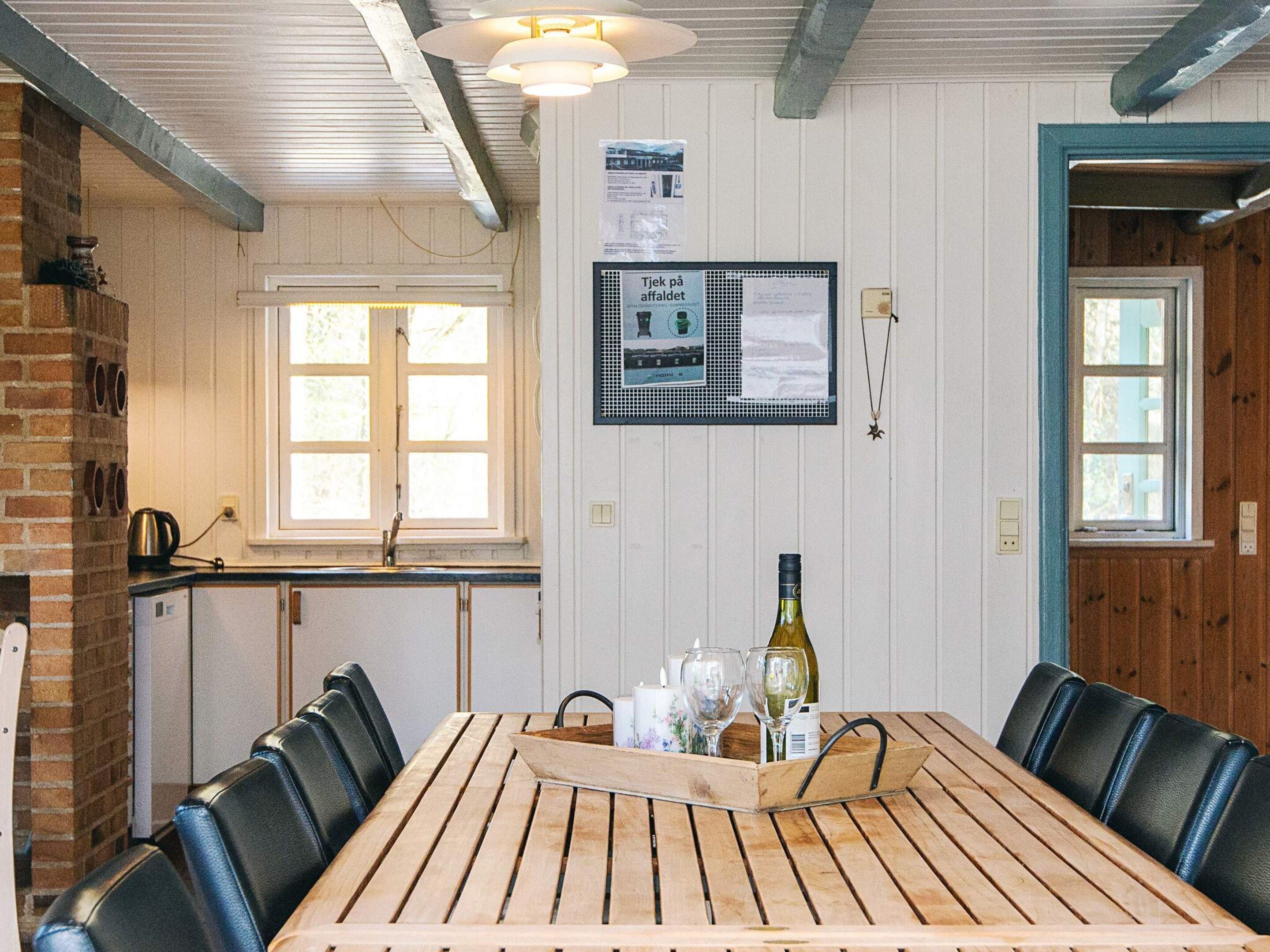 Un tavolo da pranzo in legno con sedie, una bottiglia di vino e bicchieri sopra.