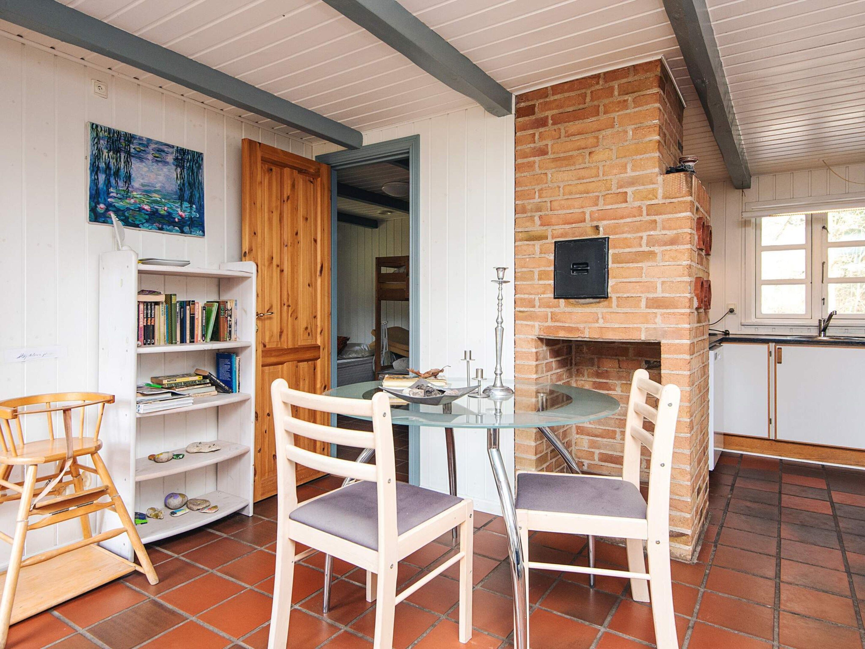 A cozy room with a glass table, two chairs, a bookshelf, a wooden door, and a brick wall with a fireplace.