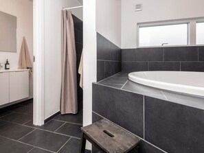 Un baño moderno con una bañera, una cortina de ducha y un taburete de madera.