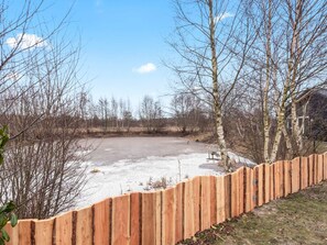 A fenced outdoor area with a paved surface, surrounded by leafless trees and a clear sky. - Holiday Home in Glesborg (Glesborg)
