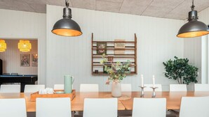 A dining area with a wooden table, white chairs, and pendant lighting. - Holiday Home in Glesborg (Glesborg)