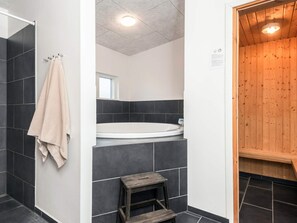 Un baño moderno con bañera, una sauna de madera y un taburete pequeño de madera.