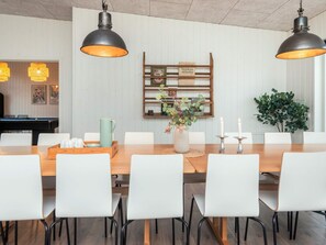 Un comedor con una mesa de madera alargada, sillas blancas e iluminación colgante.