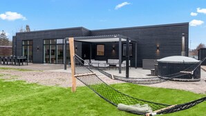 A modern building with a patio area featuring a hammock, outdoor seating, and a large water tank. - Holiday Home in Glesborg (Glesborg)