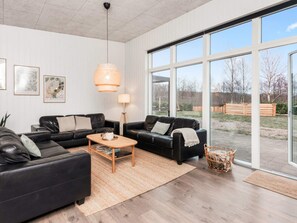 A modern living room with two black leather sofas, a wooden coffee table, and a large window offering a view of the outdoors. - Holiday Home in Glesborg (Glesborg)