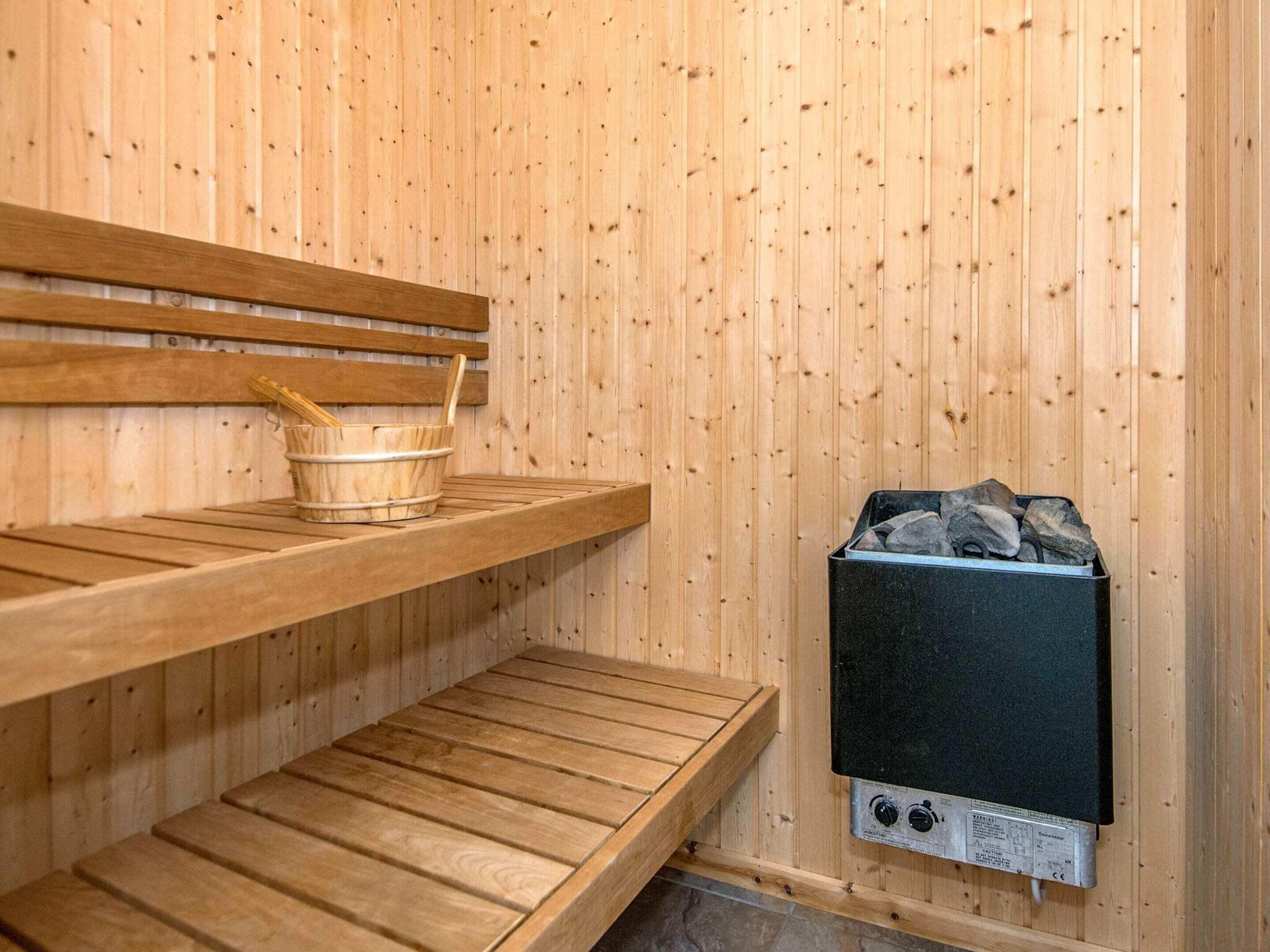 A wooden sauna with benches and a stone-filled container, likely for heating.