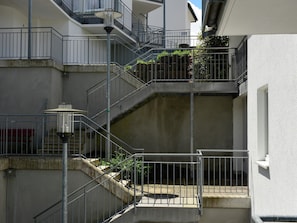 A multi-level residential building with external staircases, metal railings, and a light fixture.