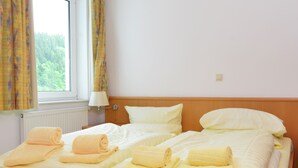 A hotel room with two beds, each with neatly folded towels, a window with curtains, and a bedside lamp. - Grosse Ferienwohnung in Willingen mit Balkon (Willingen)