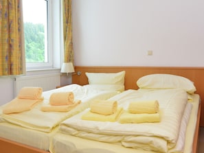 Ein Hotelzimmer mit zwei Betten, jeweils mit ordentlich gefalteten Handtüchern, einem Fenster mit Vorhängen und einer Nachttischlampe.