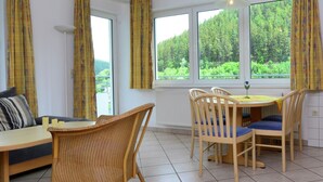 A room with a dining table, chairs, a sofa, and large windows with curtains. - Grosse Ferienwohnung in Willingen mit Balkon (Willingen)