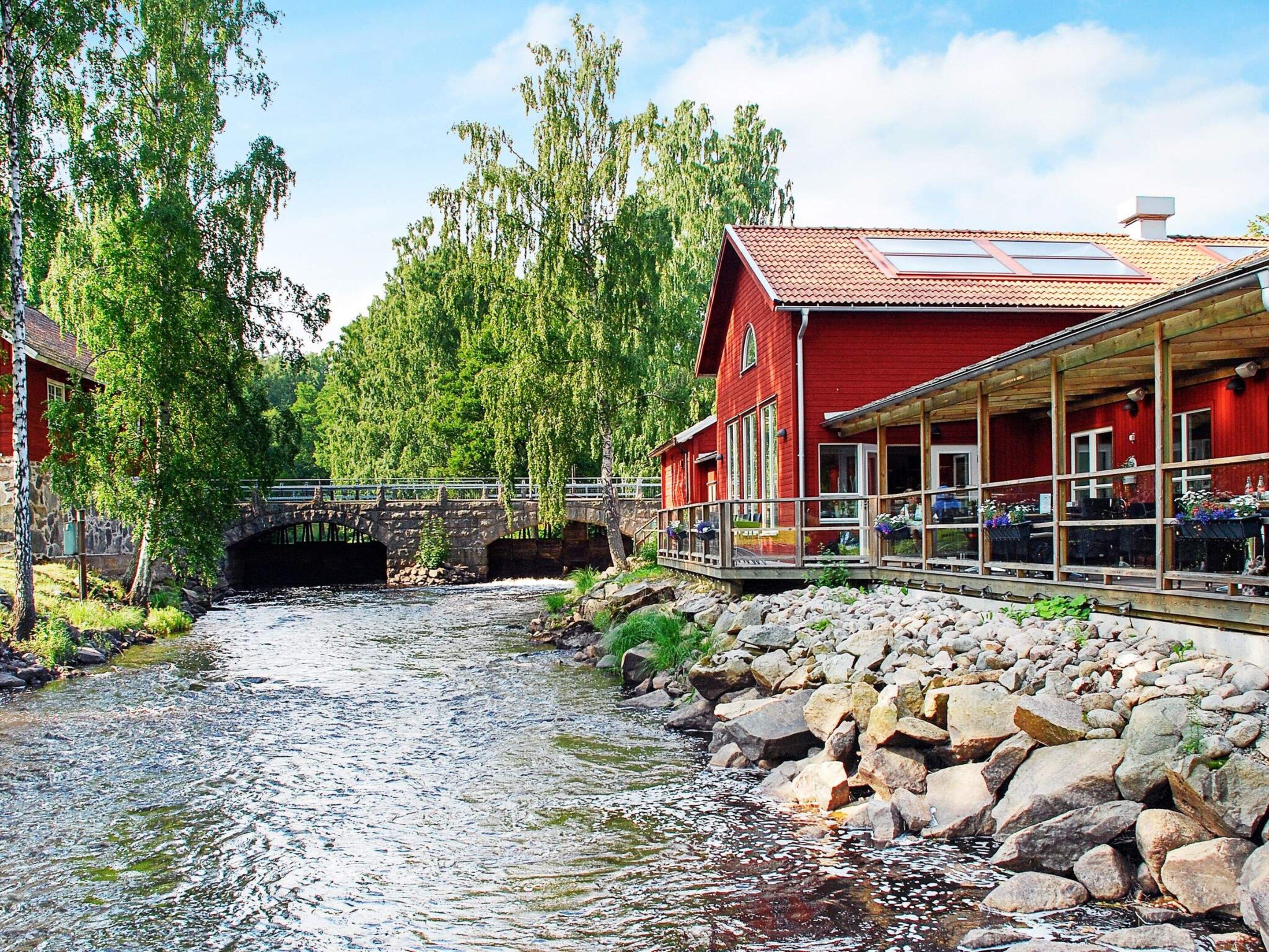 A red building with a stone bridge over a river, surrounded by greenery.