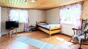 A bedroom with a wooden ceiling, a bed, a television on a stand, a chair, and a window with curtains. - 7 Person Holiday Home in Almedboda (Älmeboda)