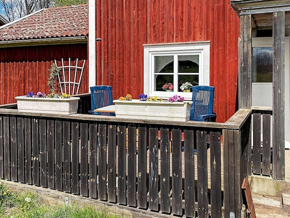 Ein rotes Holzhaus mit einem weißen Fenster und einer kleinen Veranda, auf der zwei blaue Stühle und Blumenkästen stehen.