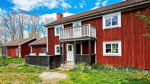 A red wooden house with a balcony, a front porch, and a small garden area. - 7 Person Holiday Home in Almedboda (Älmeboda)