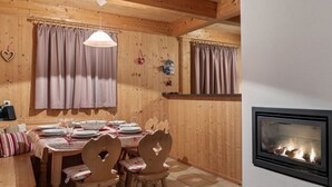 Une salle à manger en bois avec une cheminée, des chaises en bois et une table dressée pour quatre personnes.