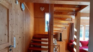 Un intérieur en bois avec un escalier menant à une mezzanine, un canapé rouge et une table sur laquelle est posée une lanterne.