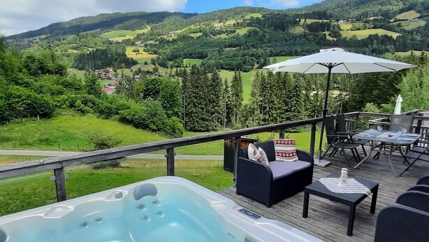 Un bain à remous sur une terrasse, agrémentée de mobilier d’extérieur et offrant une vue panoramique sur une vallée.