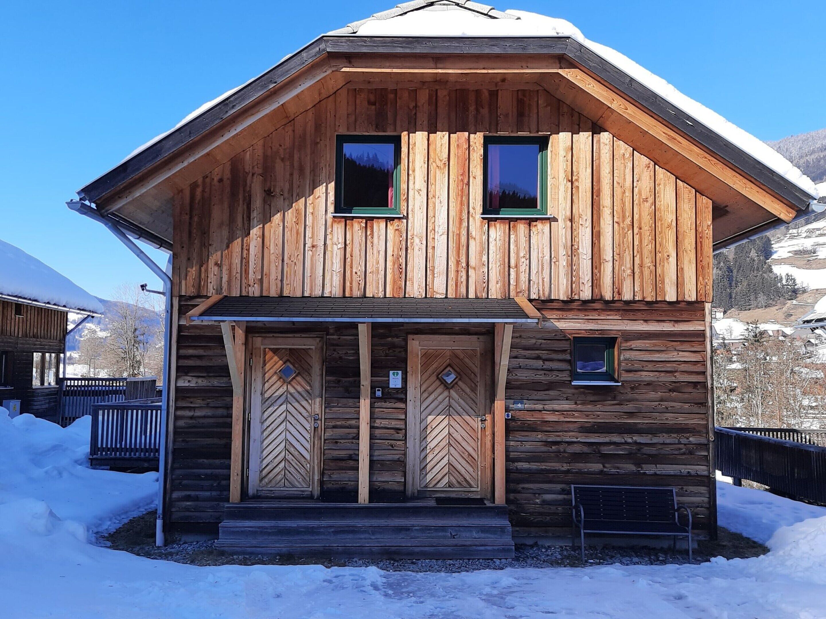 A wooden cabin with a pitched roof, two windows, and a front door with a chevron pattern.
