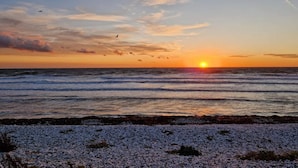 A sunset over the ocean with a pebbled beach in the foreground.