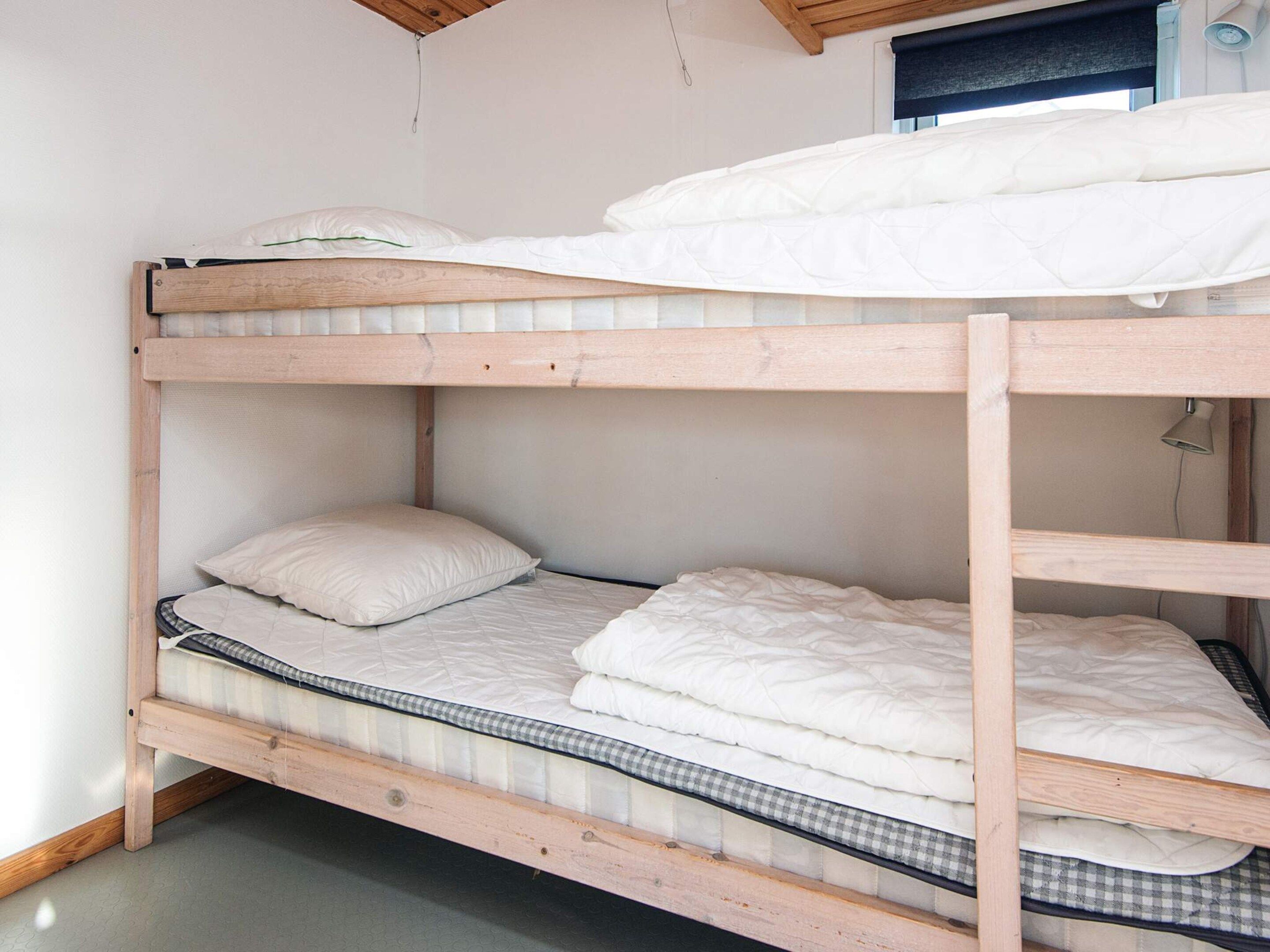 A bunk bed with a wooden frame, white bedding, and a checkered mattress cover.