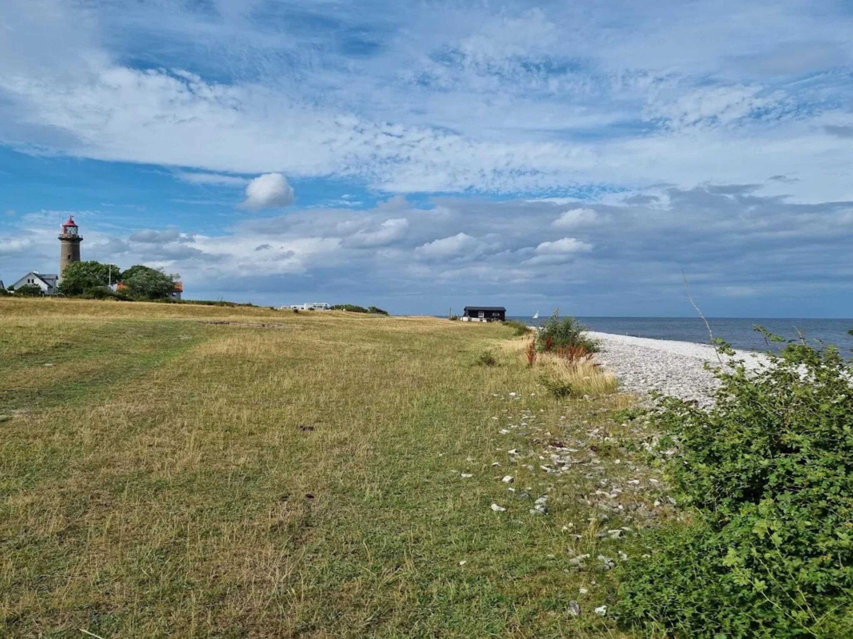 A coastal landscape with a lighthouse, grassy fields, and a beach.