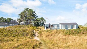 A coastal house with a dirt path leading to it, surrounded by grass and trees.
