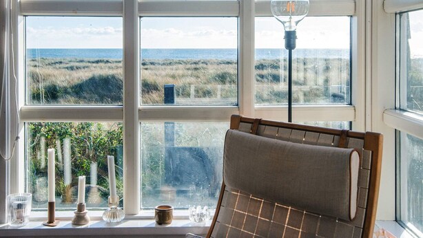 A room with a large window overlooking a beach, a lamp, and a chair.