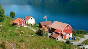 Uma vila à beira do lago com casas de telhado vermelho, uma bandeira e vista clara do lago e montanhas.