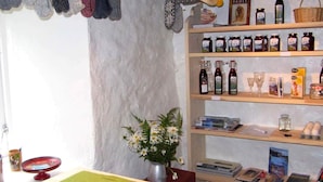 Um quarto acolhedor com uma estante repleta de livros e garrafas, uma mesa com um jogo americano verde e revistas, e um vaso com flores.