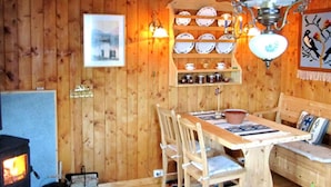 Um interior em madeira com uma mesa de jantar, cadeiras, uma lareira e prateleiras na parede com pratos e xícaras.