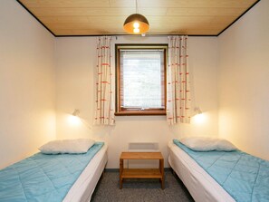 A room with two single beds, a small wooden table, a window with blinds, and two wall-mounted lamps. - 4 Person Holiday Home in Laeso (Læsø)