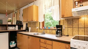 Une cuisine compacte avec des meubles en bois, un four encastré, une machine à café et une fenêtre avec des rideaux.