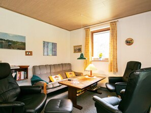 A cozy living room with a sofa, two armchairs, a coffee table, and a window with curtains.
