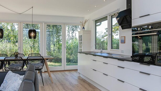 A modern kitchen with white cabinets, a black countertop, and a large window overlooking greenery. - Holiday Home in Idestrup (Idestrup)