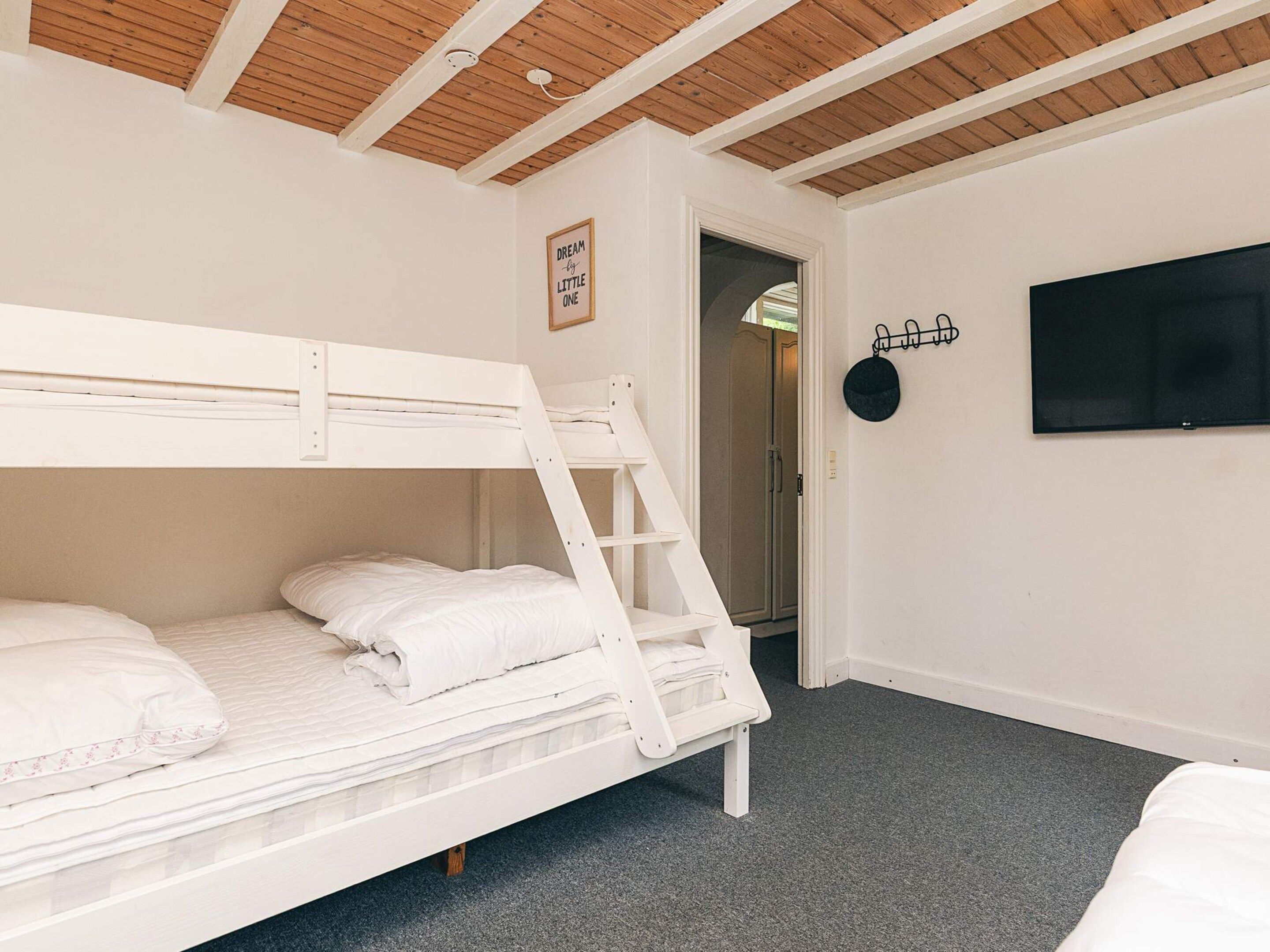 A bunk bed in a room with a wooden ceiling, a television mounted on the wall, and a door leading to another room.