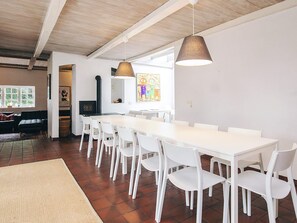 Un espace repas avec une longue table blanche et des chaises blanches, un luminaire suspendu et une fenêtre donnant sur un beau paysage.