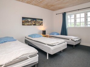 A room with two single beds, a nightstand with a lamp, a window with curtains, and a cityscape painting on the wall.