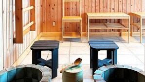 Ein Zimmer mit Holzwänden, zwei kleinen schwarzen Tischen, einer Holzbank und zwei Steinöfen.