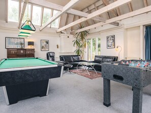 Une pièce comprenant une table de billard, un baby-foot, un canapé, un fauteuil et une grande fenêtre.