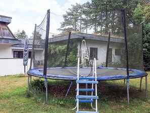 A trampoline with a safety net and ladder, surrounded by grass and trees.