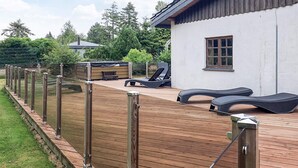 Eine Holzterrasse mit Liegestühlen und einem Whirlpool, umgeben von einem Metallzaun.