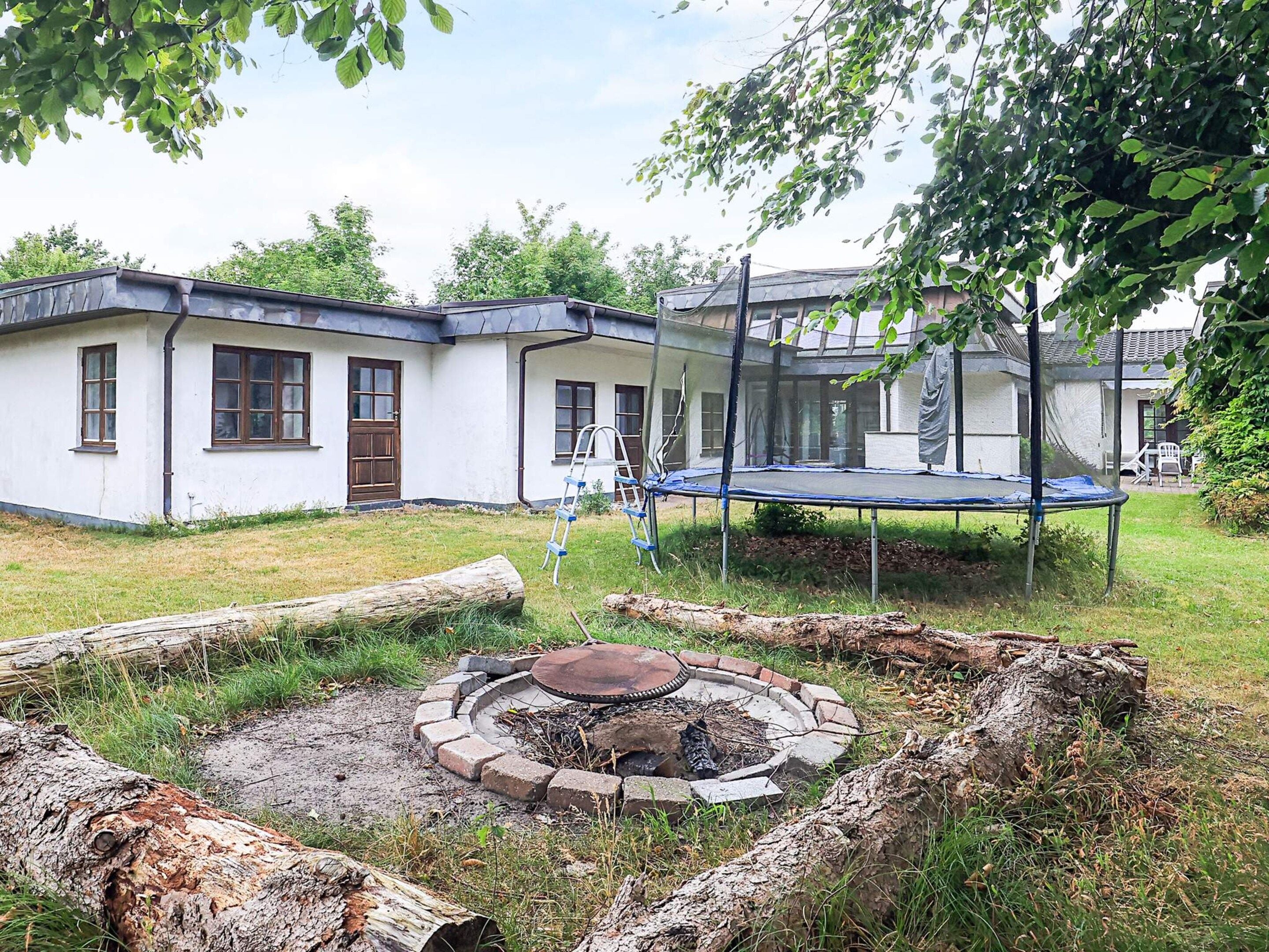 Ein Haus mit Trampolin und Feuerstelle im Garten.
