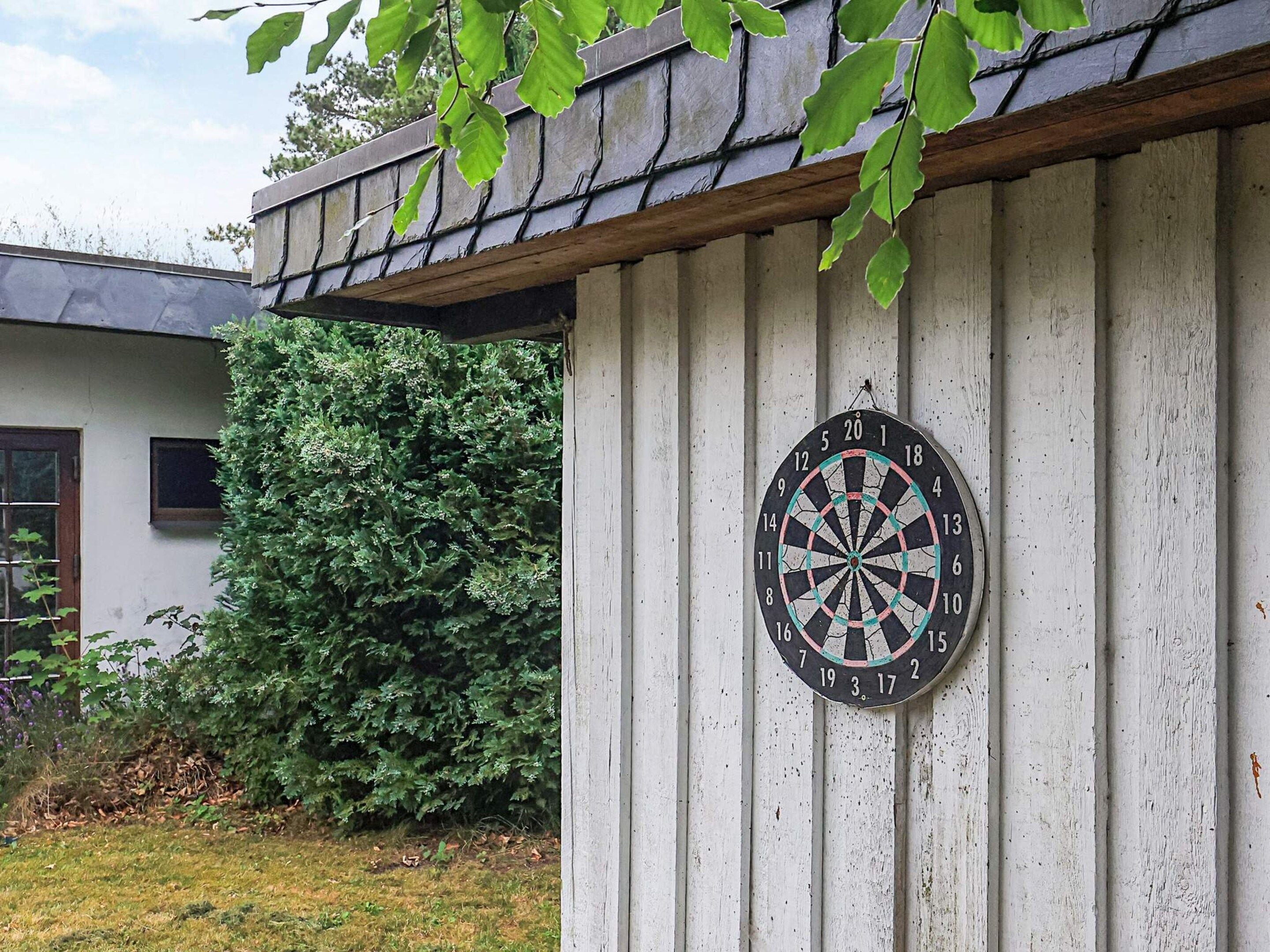 A dartboard mounted on a white wooden wall with a roof overhang.