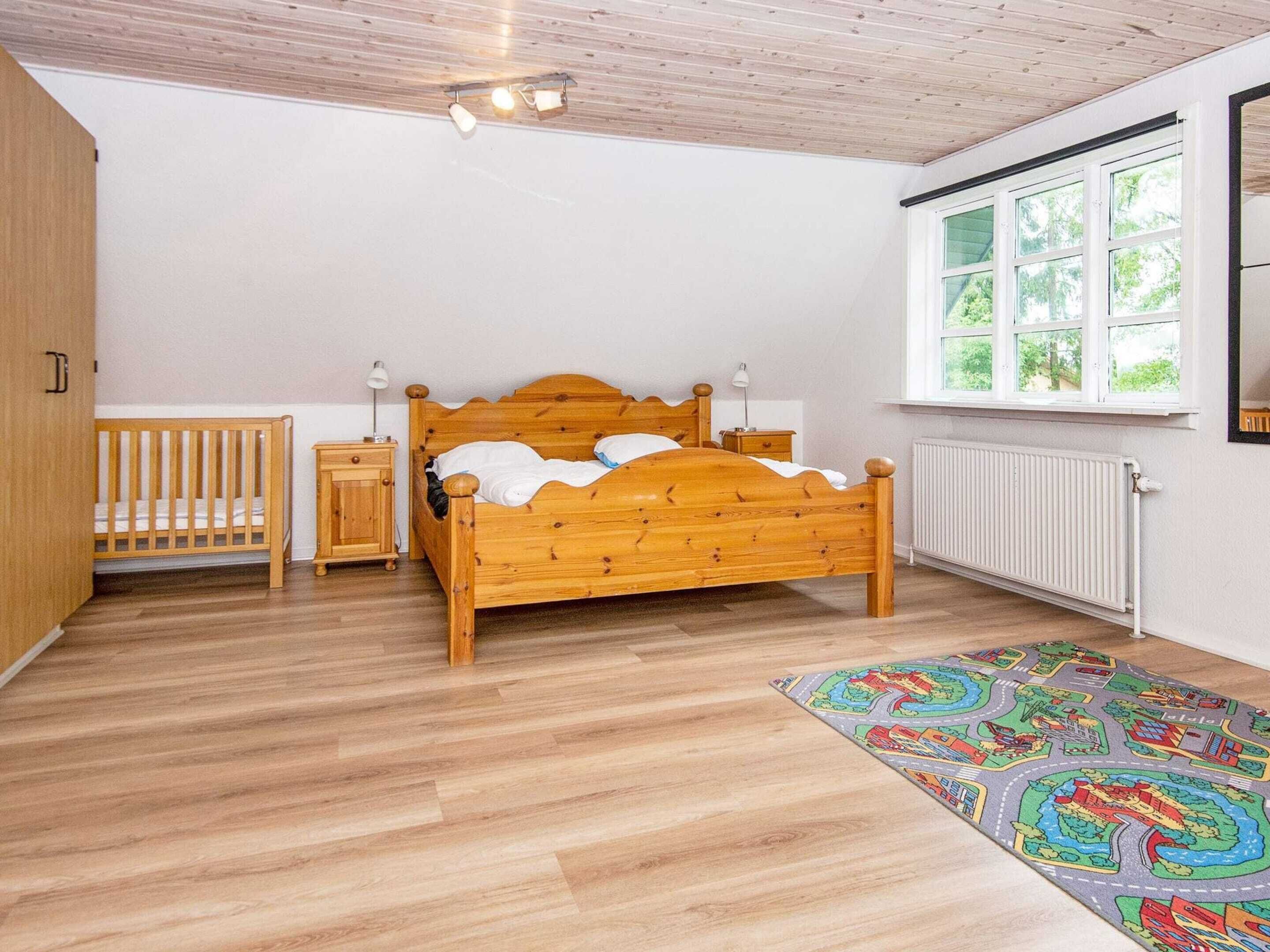A bedroom with a wooden bed, a crib, a radiator, and a window with a view of greenery.