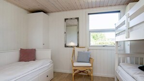 Ein Schlafzimmer mit einem Etagenbett, einem Einzelbett, einem Sessel, einem Spiegel und einem Fenster.